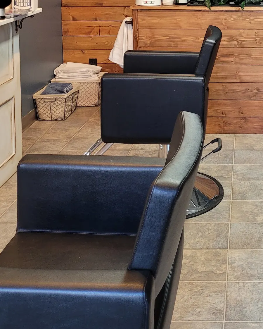The two black styling chairs on the tiled floor, towels stacked in wire baskets behind